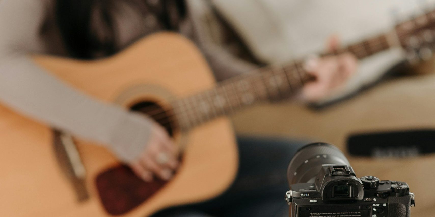Woman sitting on a couch, filming themselves playing acoustic guitar.